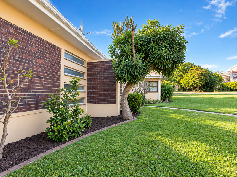 A well-maintained rear exterior view featuring a brick facade, horizontal windows, and a neatly landscaped garden with established trees and lawn.