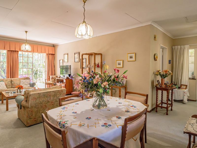 Spacious open-plan living and dining area featuring carpeted flooring, classic pendant lighting, and large french doors providing access to the garden.