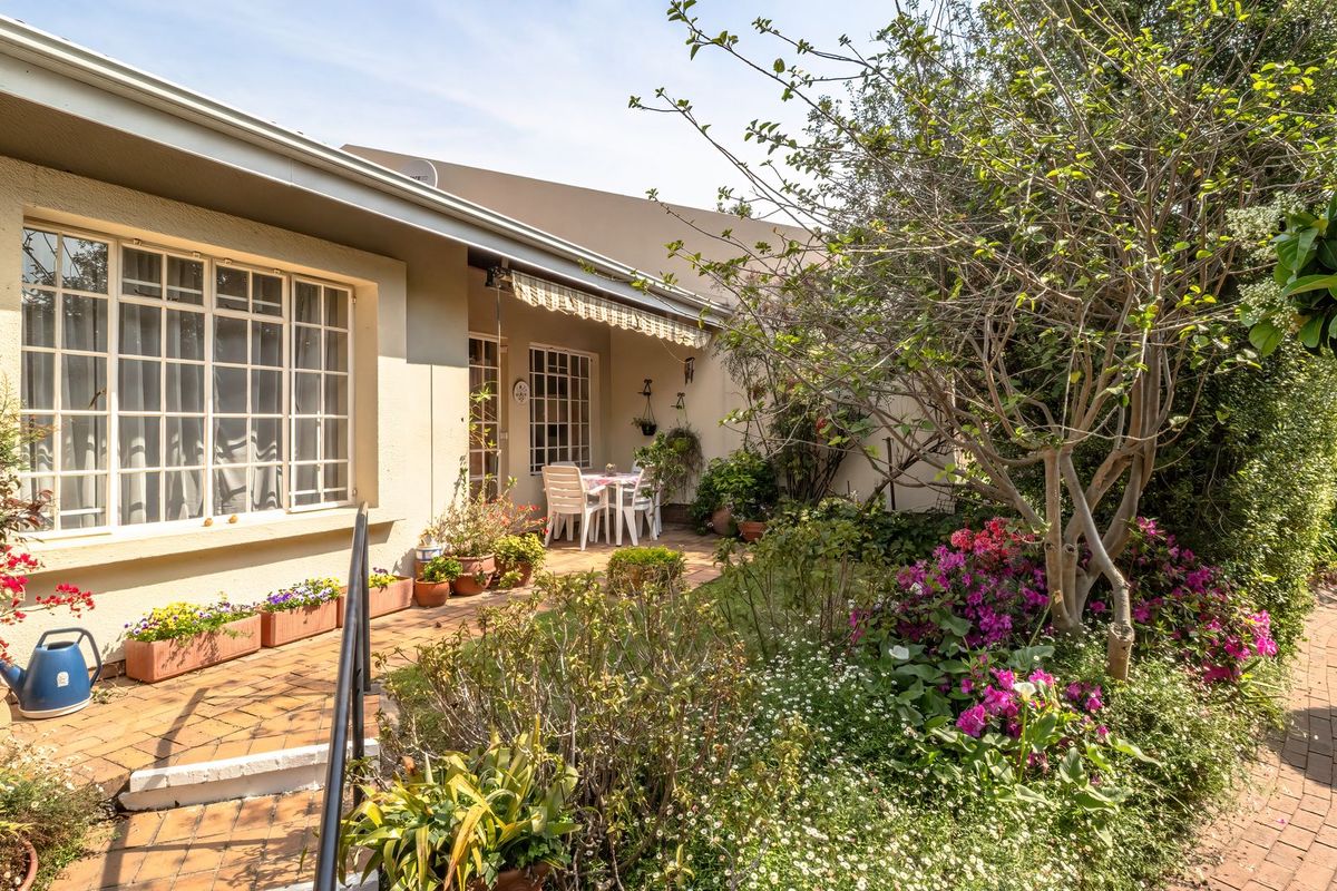 A well-maintained rear patio area featuring brick paving, a retractable awning, and established garden beds with multi-pane windows overlooking the outdoor space.