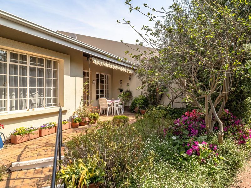 A well-maintained rear patio area featuring brick paving, a retractable awning, and established garden beds with multi-pane windows overlooking the outdoor space.