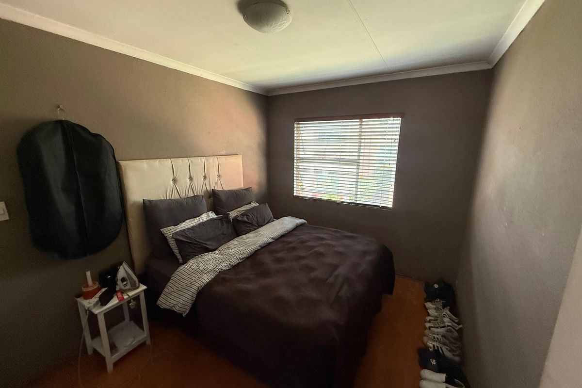 A compact bedroom featuring dark painted walls, a window with venetian blinds, and a ceiling-mounted light fixture.