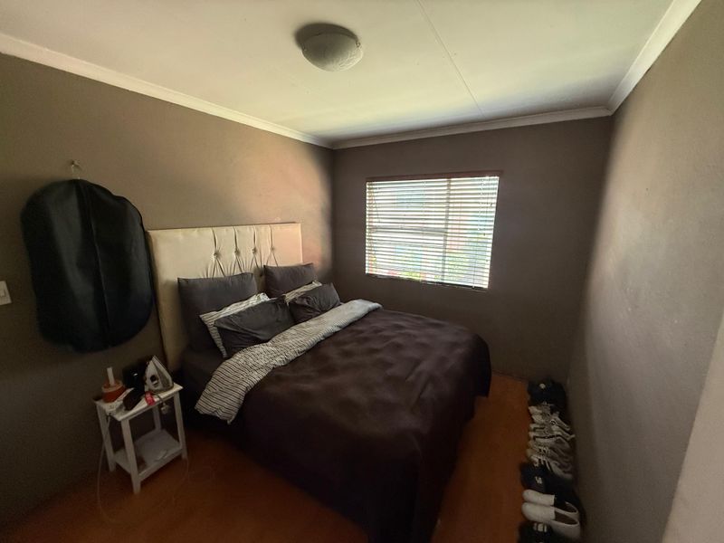 A compact bedroom featuring dark painted walls, a window with venetian blinds, and a ceiling-mounted light fixture.