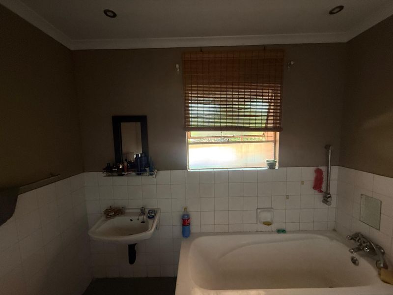 A functional bathroom featuring a built-in bathtub, wall-mounted basin, and tiled splashback, requiring some cosmetic updates to improve its overall condition.