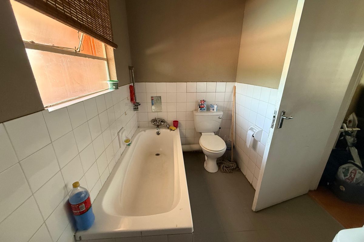 A functional bathroom featuring a standard bathtub and toilet with tiled splashbacks and a window for natural light.