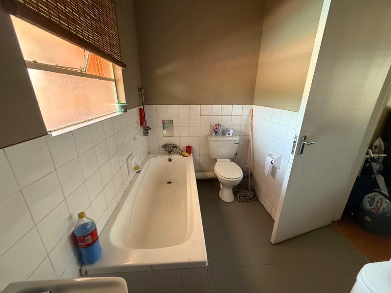 A functional bathroom featuring a standard bathtub and toilet with tiled splashbacks and a window for natural light.