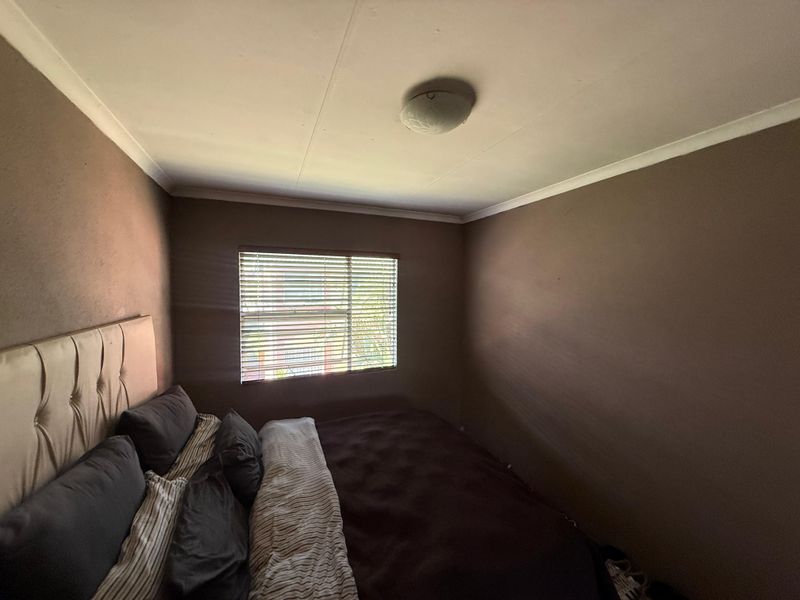 A bedroom featuring dark painted walls, a window with venetian blinds, and a central ceiling light fixture.