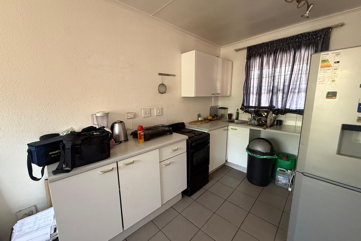 A functional kitchen featuring white cabinetry, laminate countertops, a stainless steel sink, and tiled flooring, offering potential for modernization and improved layout efficiency.