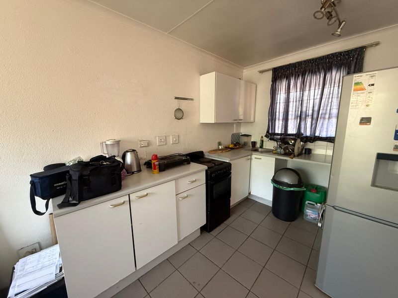 A functional kitchen featuring white cabinetry, laminate countertops, a stainless steel sink, and tiled flooring, offering potential for modernization and improved layout efficiency.