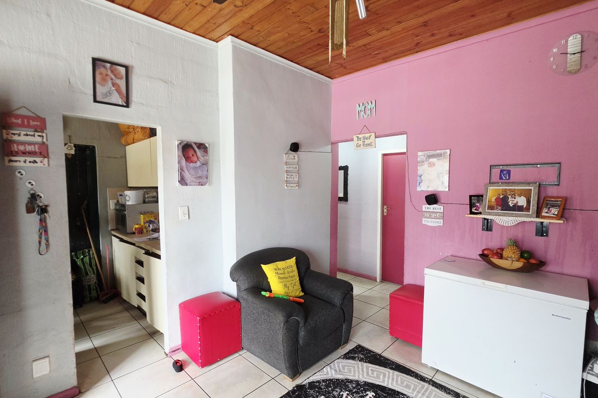 A living area featuring timber ceilings and tiled flooring, providing access to adjacent rooms and a kitchen area.