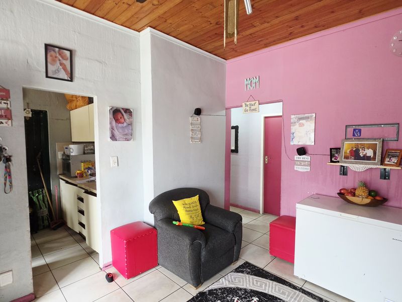 A living area featuring timber ceilings and tiled flooring, providing access to adjacent rooms and a kitchen area.