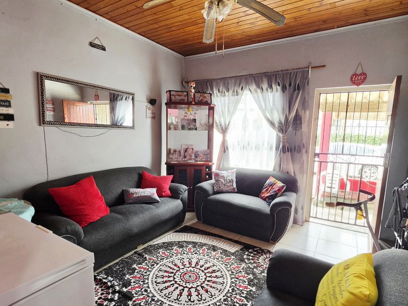 A cozy living room featuring a warm timber ceiling, ceiling fan, and tiled flooring, with direct access to the exterior through a security gate.