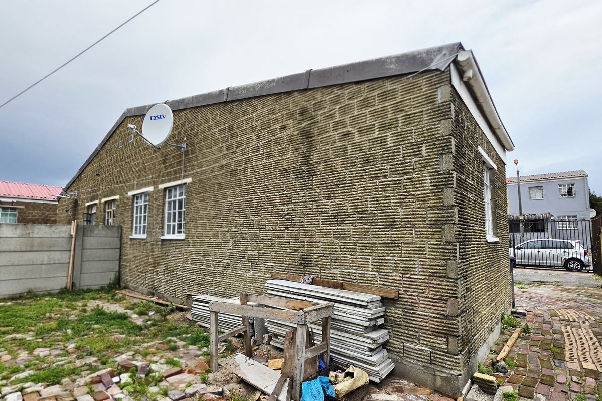 Rear exterior view of the townhouse showing textured brick walls with significant surface growth and surrounding paved area requiring maintenance.