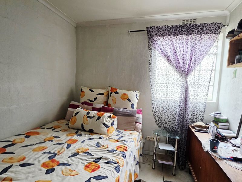 A compact bedroom featuring tiled flooring and a window, offering a functional space that could benefit from cosmetic updates to enhance its appeal.