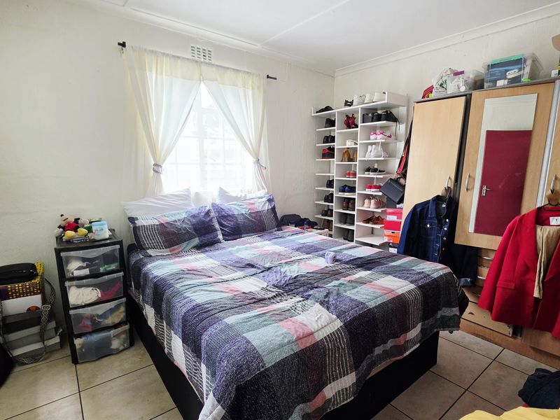 A functional bedroom featuring tiled flooring, a built-in wardrobe, and a dedicated shelving unit for storage.