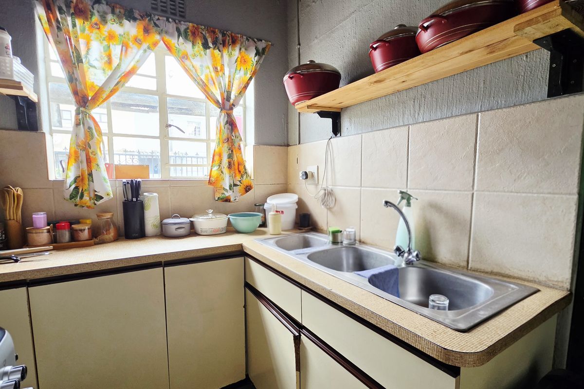 A functional kitchen area featuring a double bowl stainless steel sink, laminate countertops, tiled splashback, and timber wall shelving.