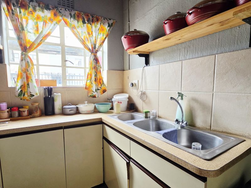 A functional kitchen area featuring a double bowl stainless steel sink, laminate countertops, tiled splashback, and timber wall shelving.