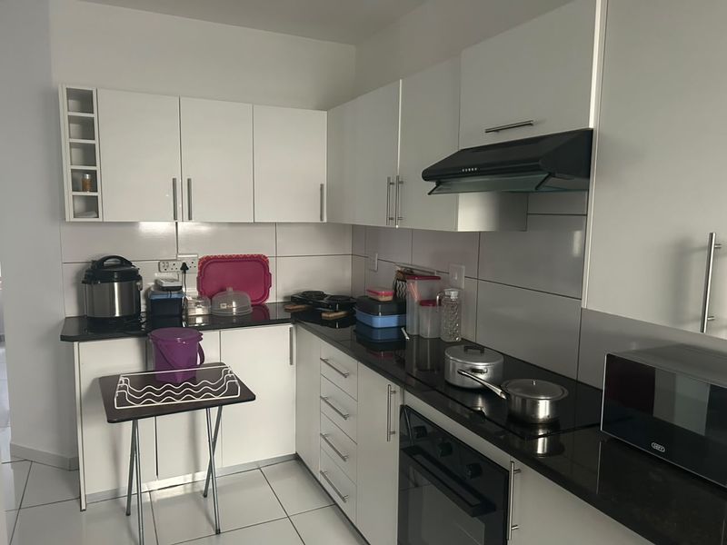 A functional kitchen featuring white cabinetry, black granite countertops, a built-in oven, electric hob, and a modern extractor fan with tiled finishes.