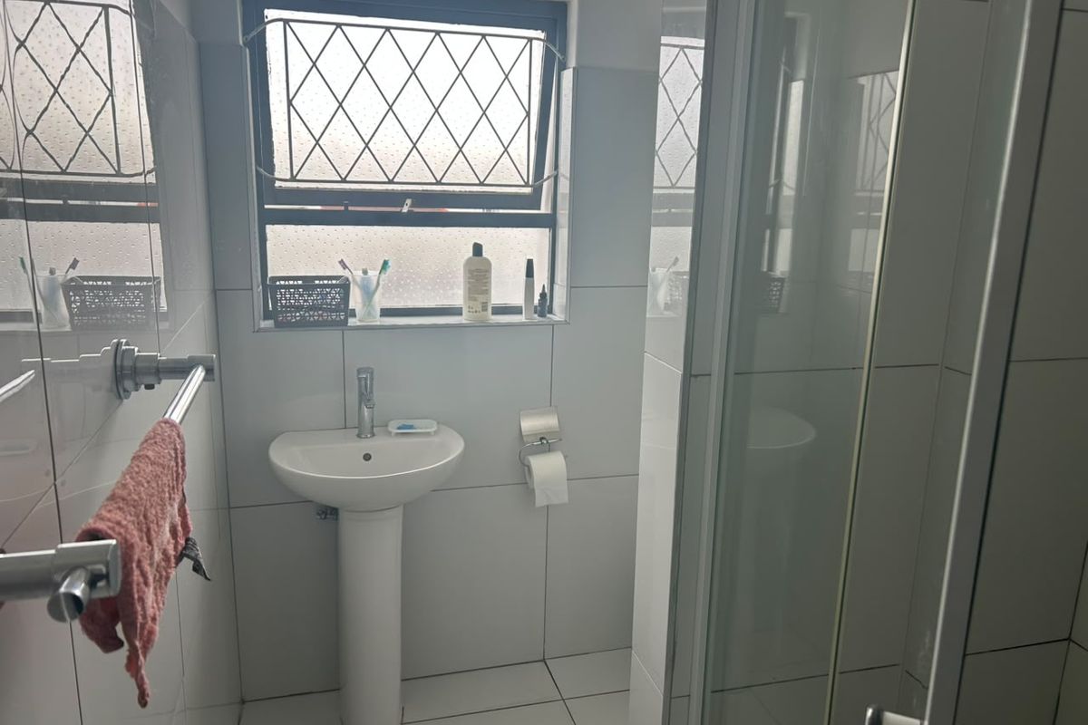 A functional bathroom featuring a pedestal basin, tiled finishes, and a glass shower enclosure with a leaded window.