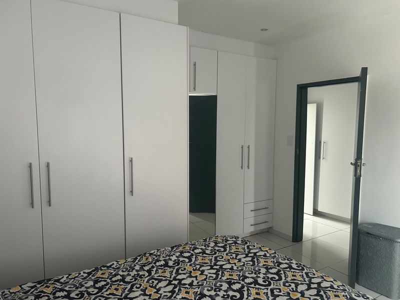 A bedroom featuring modern white built-in cupboards with sleek handles and neutral tiled flooring, providing ample storage space.