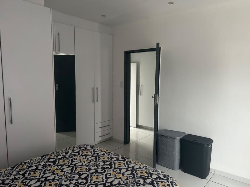 A bedroom featuring white built-in cupboards, tiled flooring, and recessed downlighting, offering a clean and functional living space.
