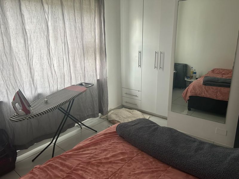 A bedroom featuring tiled flooring, a built-in wardrobe with white cabinetry, and a large wall-mounted mirror.