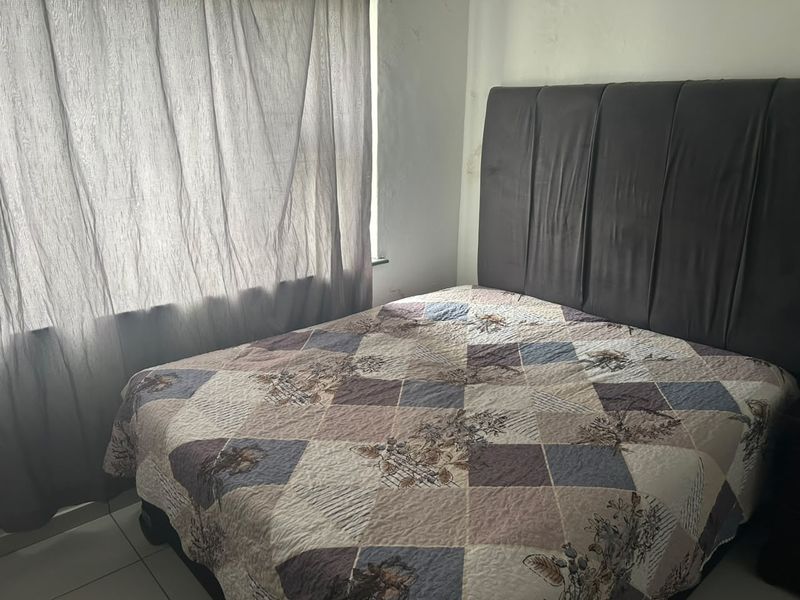 A bedroom featuring tiled flooring and a window with curtains, showing signs of wall staining that may require maintenance.