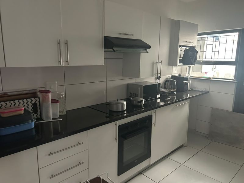 Modern kitchen featuring white cabinetry, black granite countertops, integrated oven and hob, tiled backsplash, and a window with security bars.