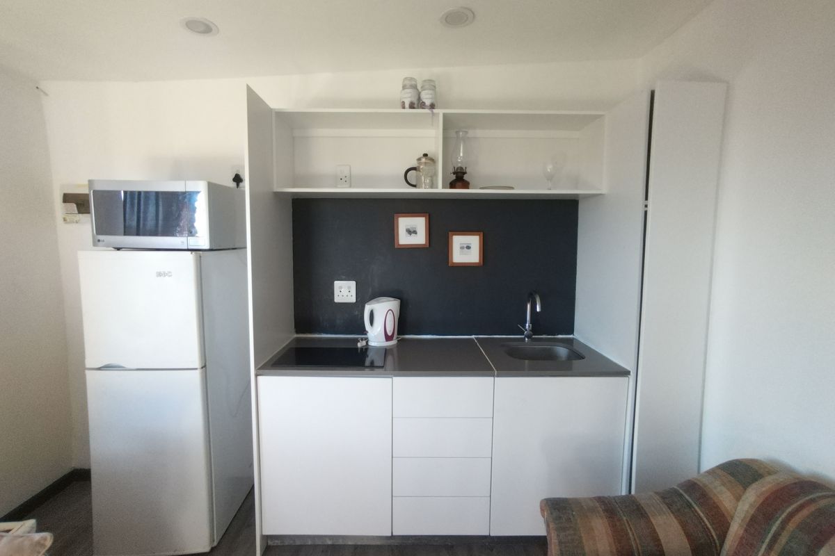 Compact kitchenette featuring white cabinetry, a dark backsplash, integrated sink, and hob, providing essential functionality in a small apartment space.