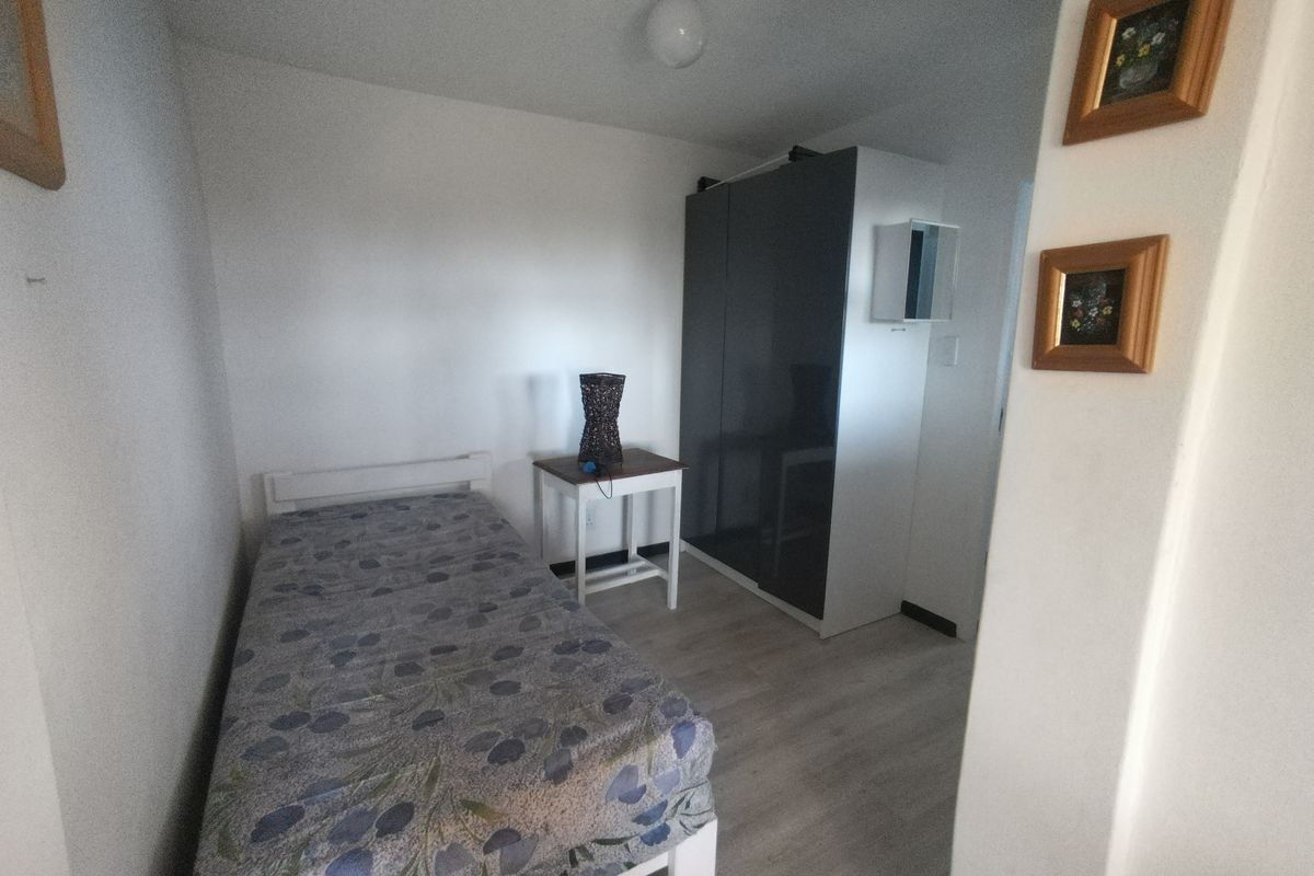 A compact bedroom featuring light-toned laminate flooring and a modern dark-toned built-in wardrobe.