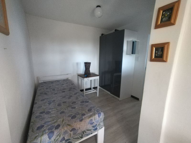 A compact bedroom featuring light-toned laminate flooring and a modern dark-toned built-in wardrobe.