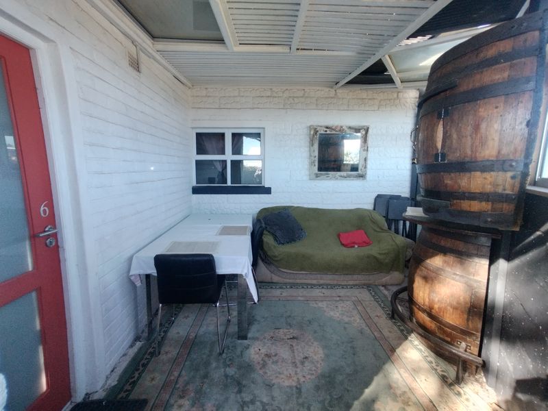 A covered outdoor patio area featuring painted brick walls and a slatted ceiling, providing a functional space for outdoor relaxation.