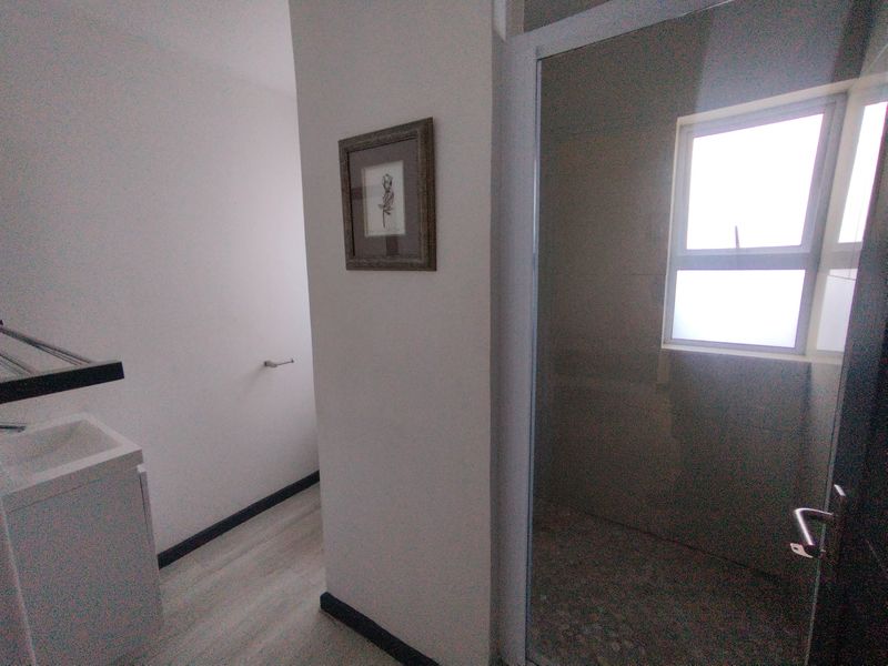 A modern bathroom featuring a glass-enclosed shower, vanity basin, and neutral tiled flooring with natural light from a window.