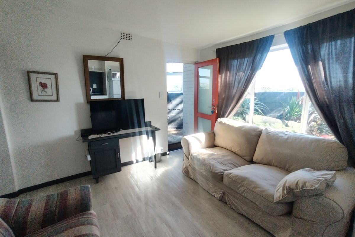 A bright living room featuring light-toned laminate flooring, large windows allowing natural light, and direct access to an outdoor area.