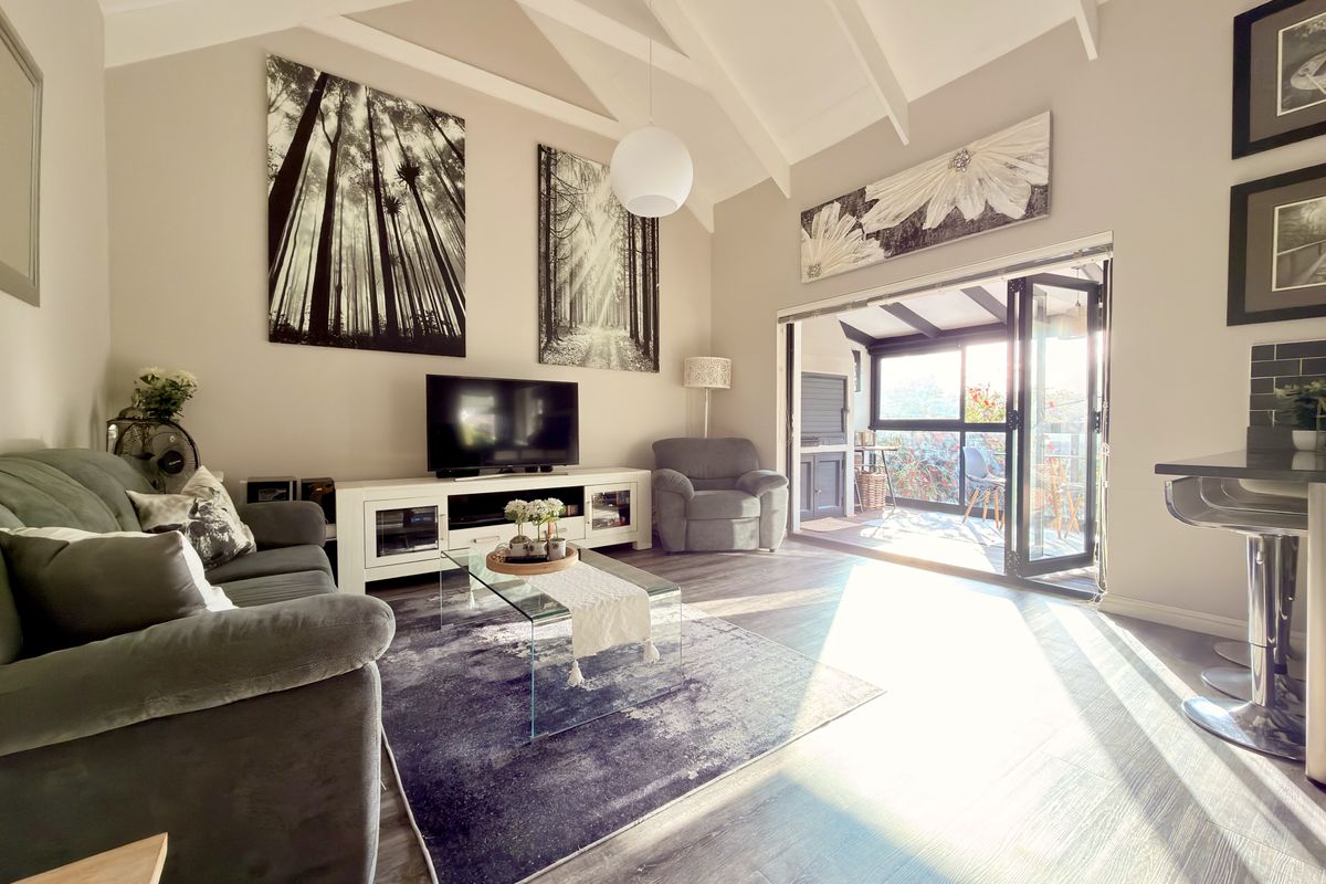 Bright living room featuring a vaulted ceiling with exposed rafters, laminate flooring, and bi-fold doors opening onto an outdoor patio area.