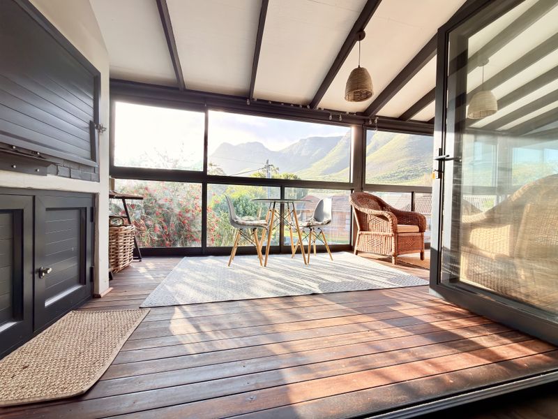 A covered patio featuring timber decking, a built-in braai, and expansive glass windows offering scenic mountain views.