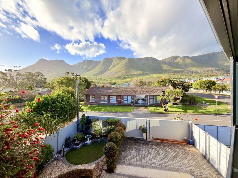 Elevated view overlooking a residential street, paved driveway, and well-maintained garden with a scenic mountain backdrop.