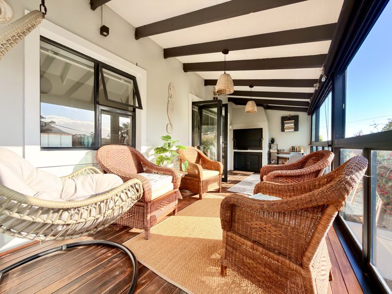 A covered patio featuring timber decking, exposed ceiling beams, and a glass-enclosed perimeter, offering a bright and inviting outdoor living space.