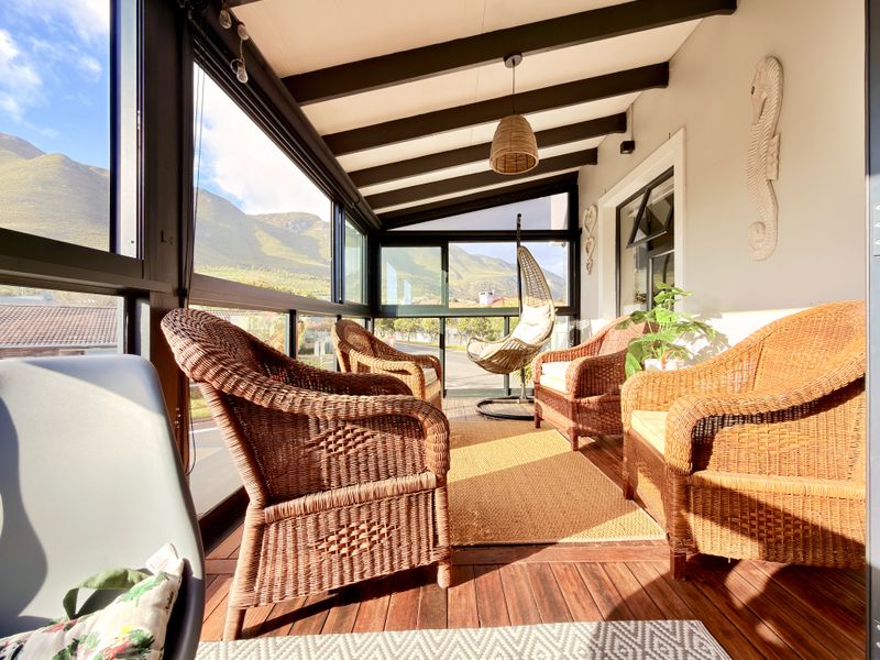 A bright, enclosed patio featuring timber decking, exposed ceiling beams, and large glass windows offering scenic mountain views.