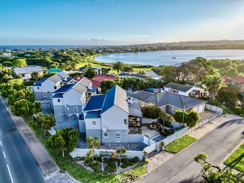 Aerial view of a townhouse property featuring a modern pitched roof, paved driveway, and private patio, situated in a scenic coastal residential area.