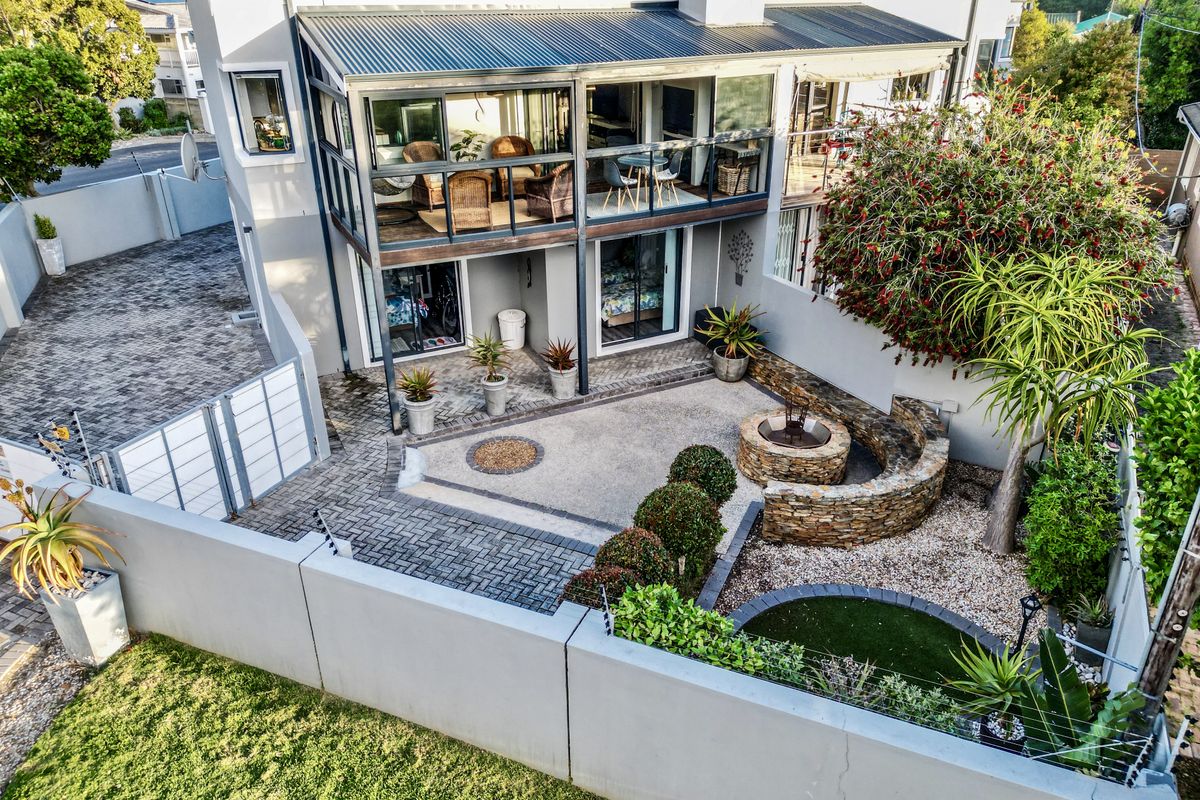 Rear view of the townhouse featuring a paved courtyard, stone fire pit, and an enclosed upper-level balcony with sliding glass doors.