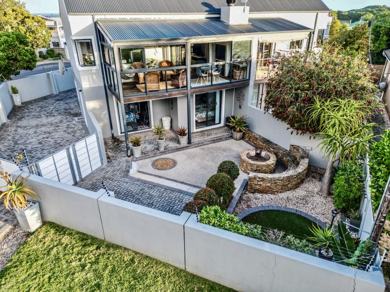Rear view of the townhouse featuring a paved courtyard, stone fire pit, and an enclosed upper-level balcony with sliding glass doors.