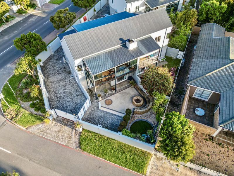Aerial view of a modern townhouse featuring a corrugated metal roof, paved driveway, private balcony, and a landscaped courtyard with a stone fire pit.