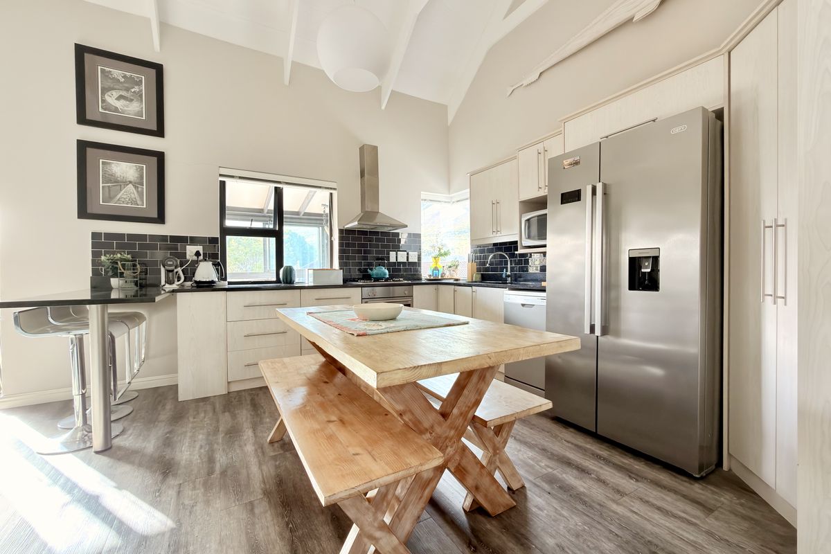 Modern kitchen featuring vaulted ceilings, dark subway tile backsplash, ample cabinetry, and high-quality laminate flooring in a bright, open-plan layout.