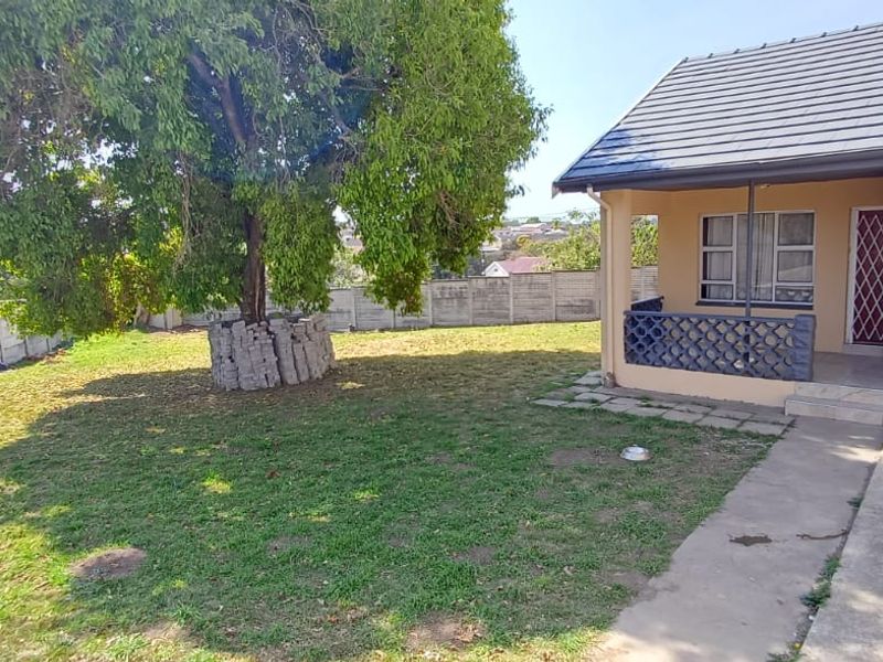 Rear garden area featuring a covered patio, brick braai, and perimeter precast walling with established trees.