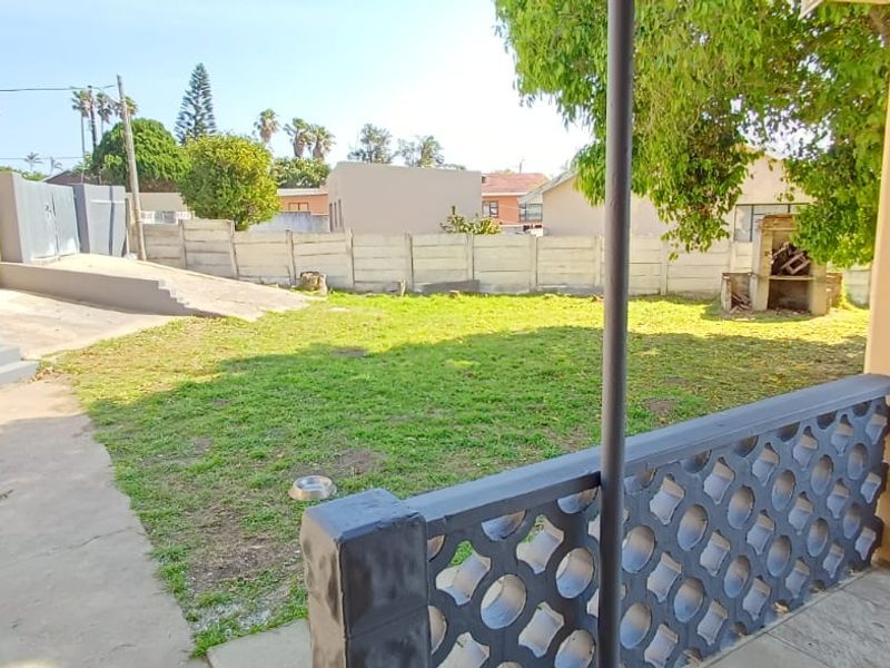 A rear garden view featuring a covered patio with decorative breeze block balustrades, a built-in braai, and a concrete ramp leading to the yard.