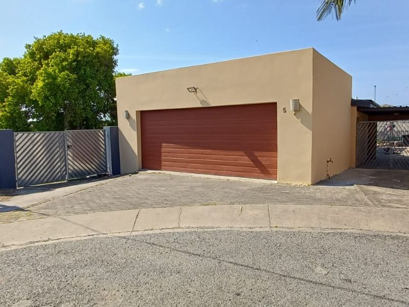 Front exterior view of the property featuring a single garage with a wood-look door, paved driveway, and secure gated access.