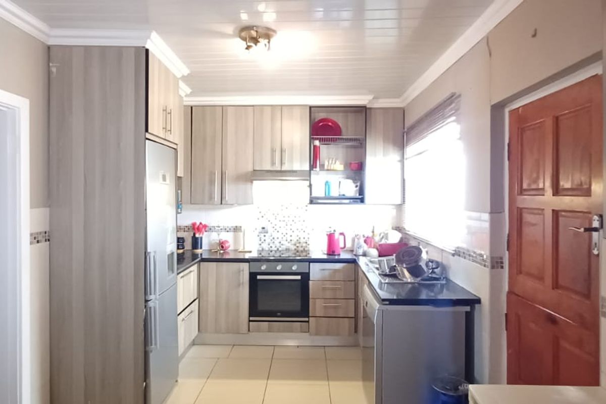 Functional kitchen featuring wood-look cabinetry, dark countertops, tiled backsplash, and built-in oven with hob, offering a practical layout for daily meal preparation.