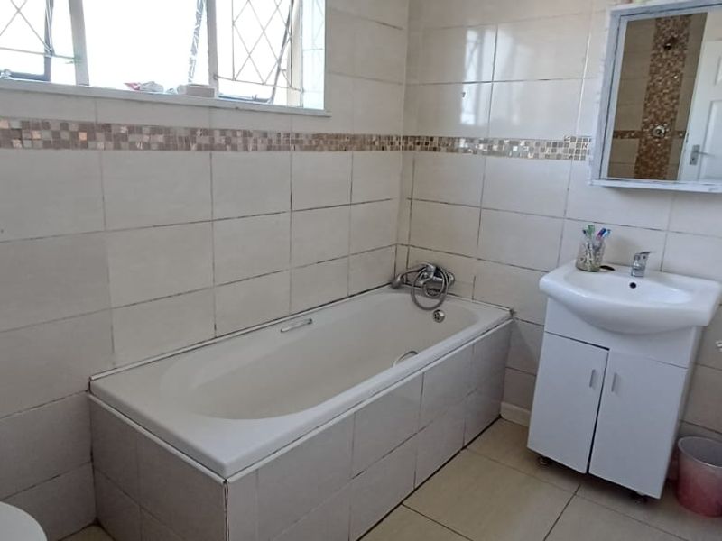 A functional bathroom featuring a built-in bathtub, vanity basin, and neutral wall tiling with decorative mosaic accents.
