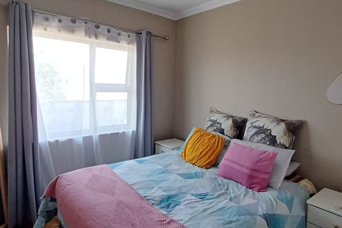 A functional bedroom featuring laminate flooring, neutral wall tones, and a large window providing natural light.