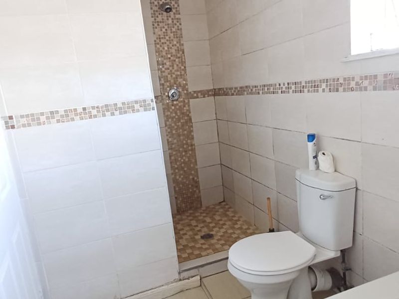 A functional bathroom featuring a walk-in shower with mosaic tile accents, a standard toilet, and neutral wall tiling throughout.